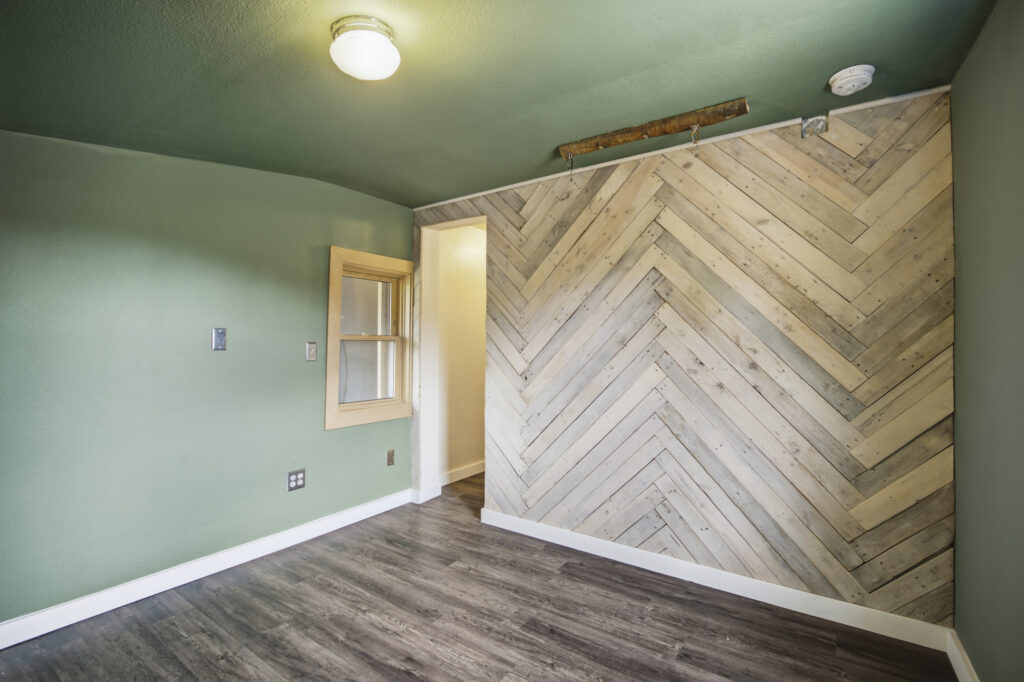 Remodeled back room at 4616 Cliff View Lane Fort Collins with herringbone reclaimed wood accent wall, sage green walls, and new vinyl plank flooring